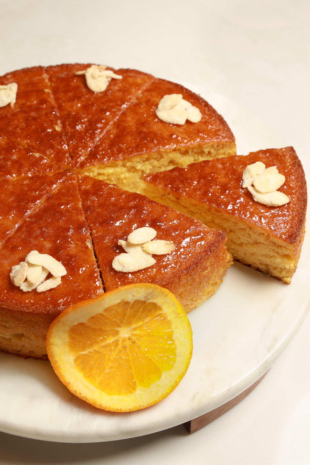 Orange almond cake sliced on a marble stand with a candied orange slice