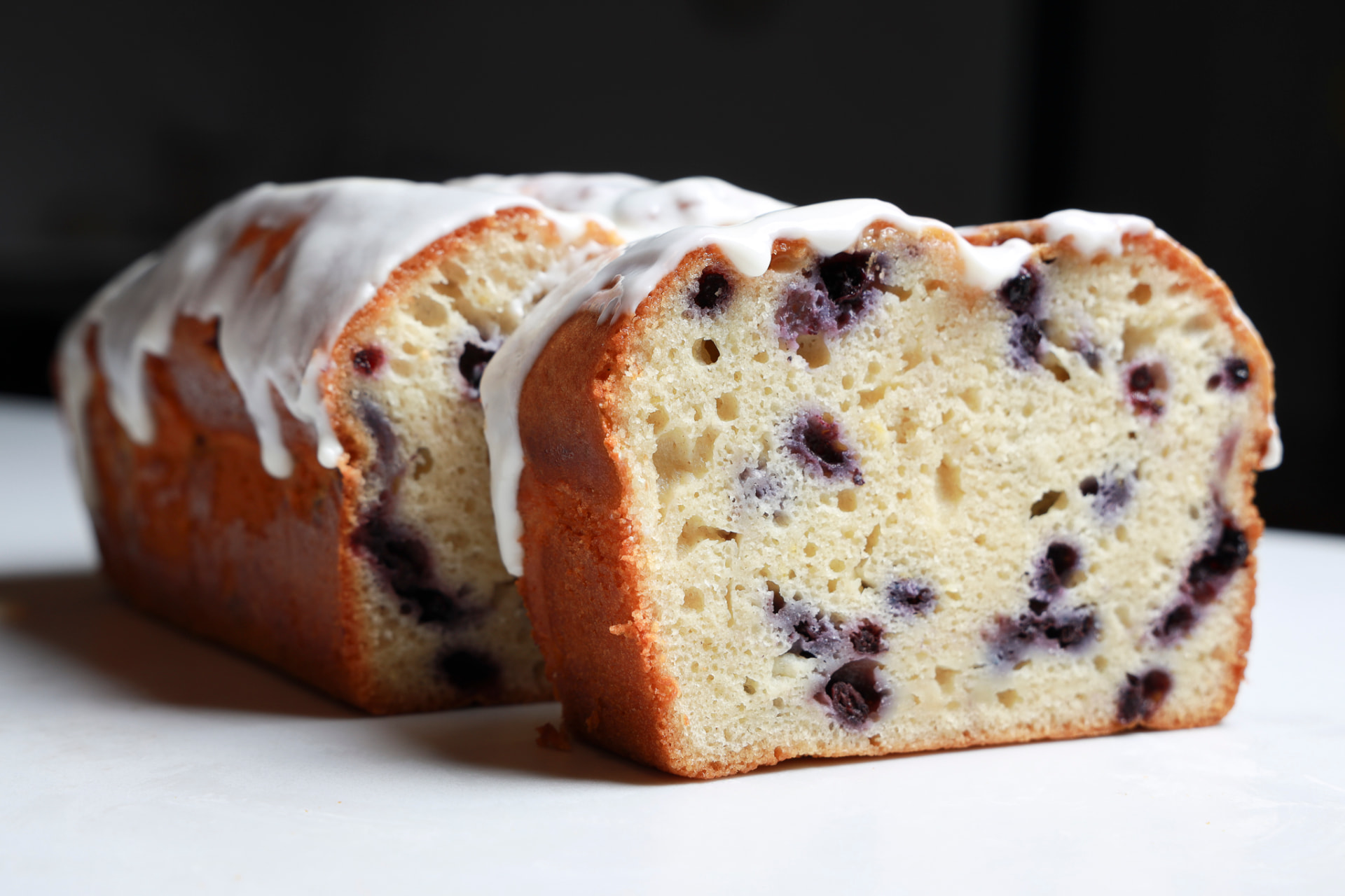 Glazed lemon blueberry loaf cake sliced on a wooden board with fresh blueberries