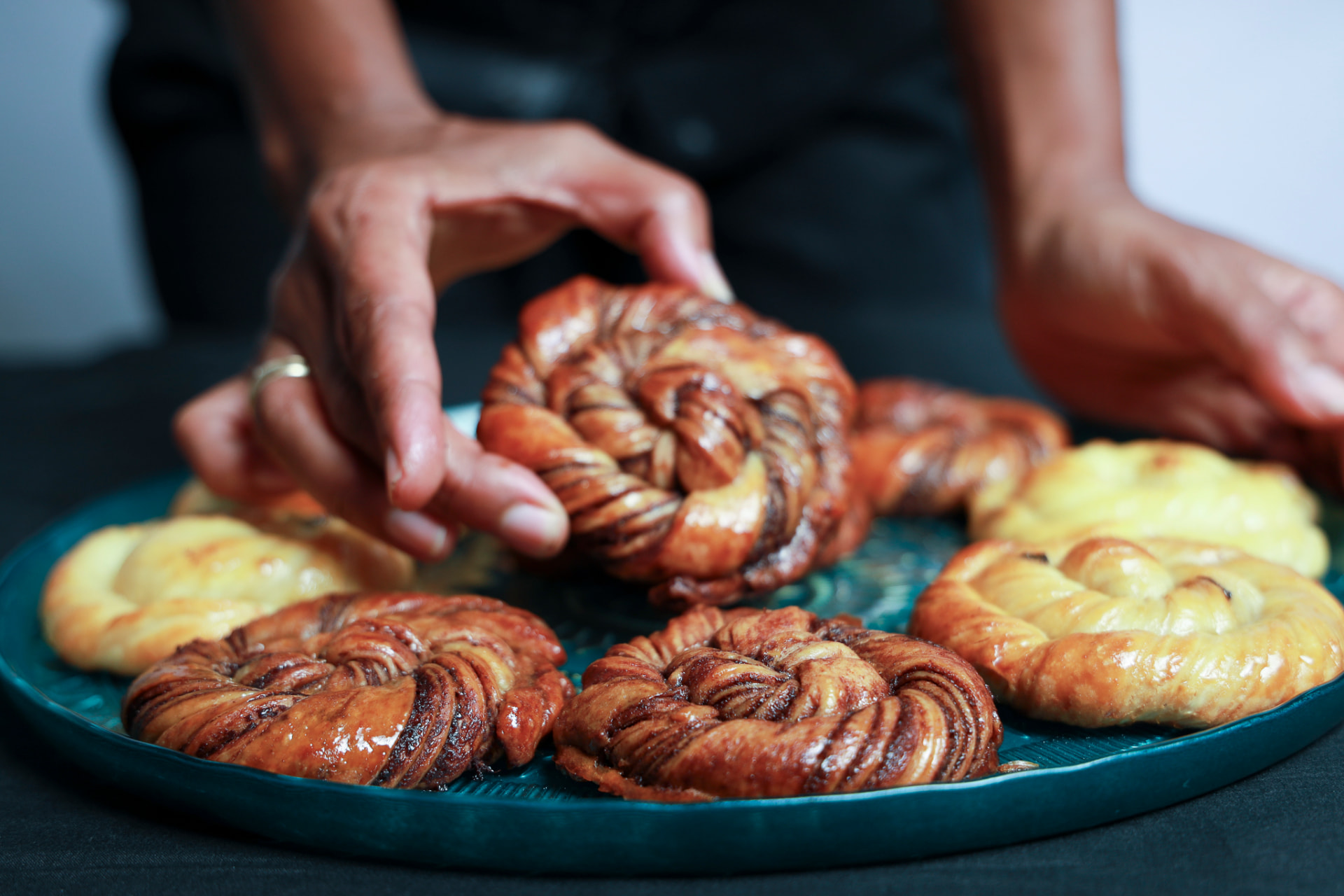Hands arranging freshly baked twists on a teal serving plate