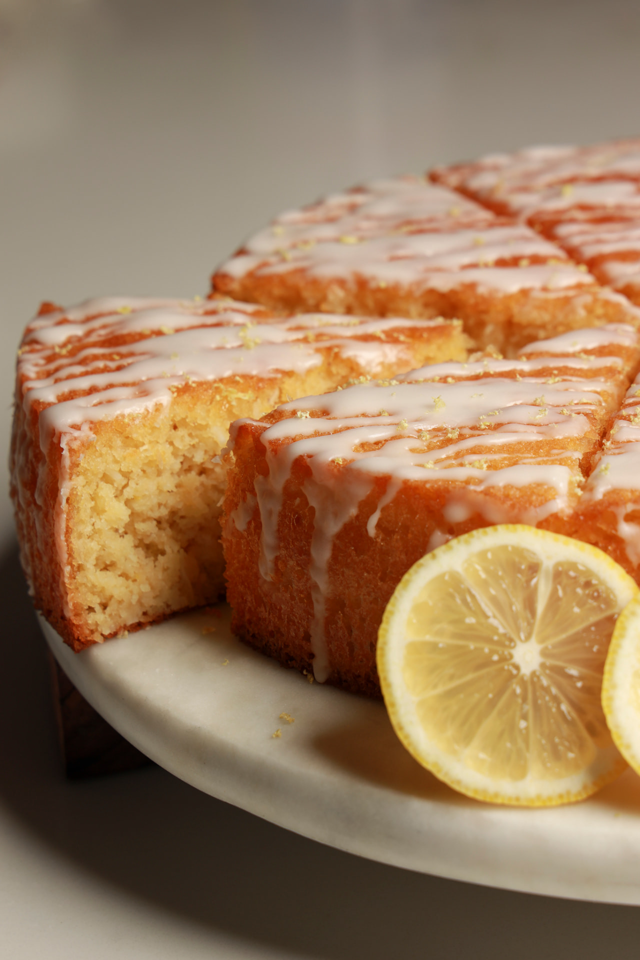 Glazed lemon cake sliced on a marble stand with fresh lemon slices